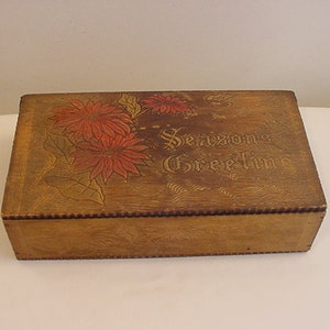 May include: A wooden box with a floral design and the text "Seasons Greetings" on the lid. The box is painted in shades of brown, red, and green.