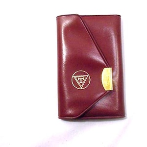 May include: A burgundy leather wallet with a gold clasp and a gold triangle with the letter "T" inside.
