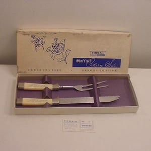 Puede incluir: Una caja blanca con una etiqueta azul y blanca que dice "Sheffield Cutlery Set" y "Guaranteed Forever Sharp". La caja contiene un cuchillo y un tenedor con mangos blancos.