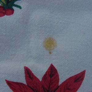 May include: A white fabric with a small yellow stain. The fabric has a red and green floral pattern.
