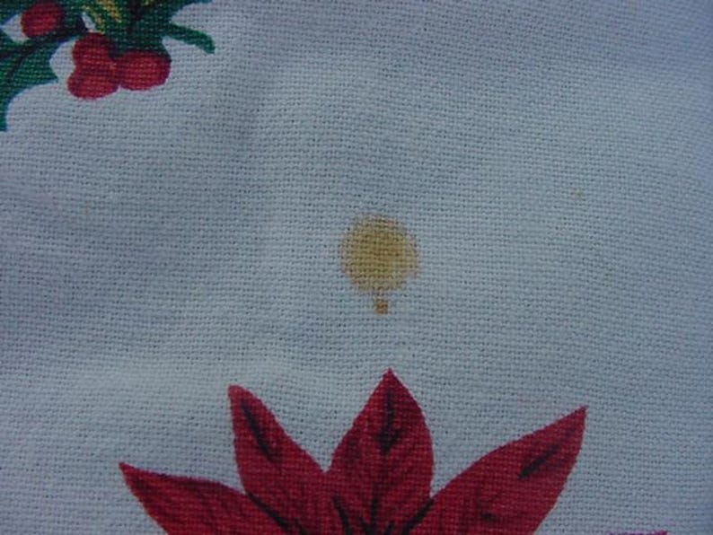 May include: A white fabric with a small yellow stain. The fabric has a red and green floral pattern.