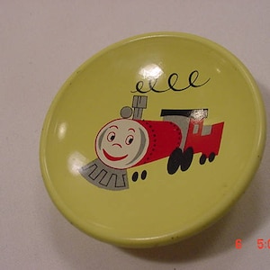 Könnte beinhalten: Ein gelber Keramikteller mit einem Cartoon-Zugdesign. Der Zug ist rot mit einem schwarzen und grauen Schornstein und Rädern. Der Zug hat ein lächelndes Gesicht und die Worte "eeee" sind darüber geschrieben.