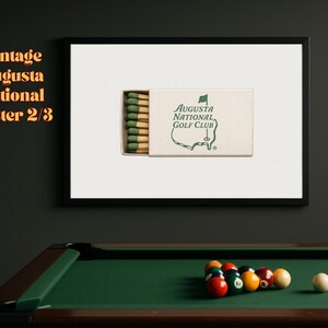 May include: A vintage poster featuring a box of matches with the Augusta National Golf Club logo. The poster is framed and hanging on a wall above a pool table.