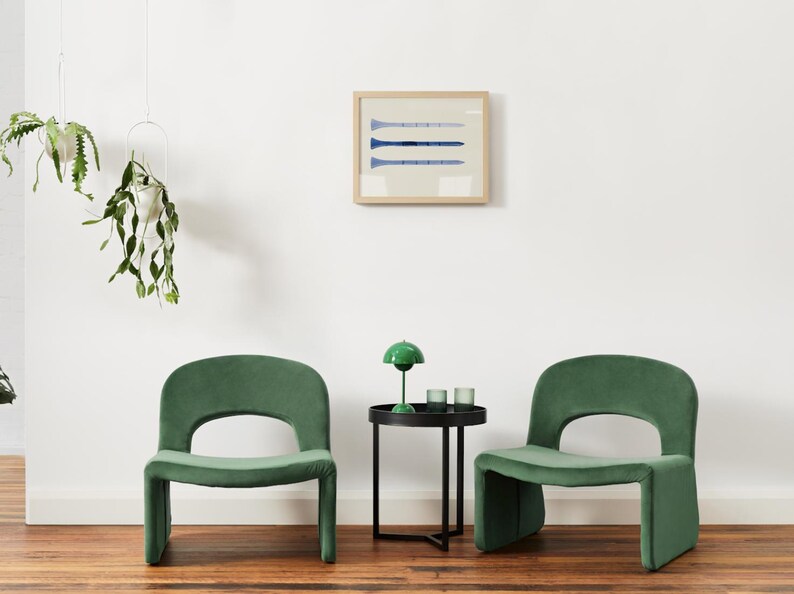 Puede incluir: Dos sillas de terciopelo verde con una mesa auxiliar negra entre ellas. La mesa tiene una l&aacute;mpara verde con una pantalla blanca y dos candelabros de vidrio transparente. Las sillas tienen un dise&ntilde;o &uacute;nico con un respaldo curvo y un asiento ancho.