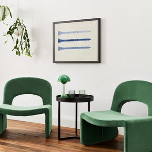 Puede incluir: Dos sillas de terciopelo verde con una mesa auxiliar de metal negro entre ellas. La mesa tiene una l&aacute;mpara verde con una pantalla blanca y dos vasos de vidrio transparente. Una impresi&oacute;n enmarcada con tres l&iacute;neas azules sobre un fondo blanco cuelga de la pared detr&aacute;s de la mesa.
