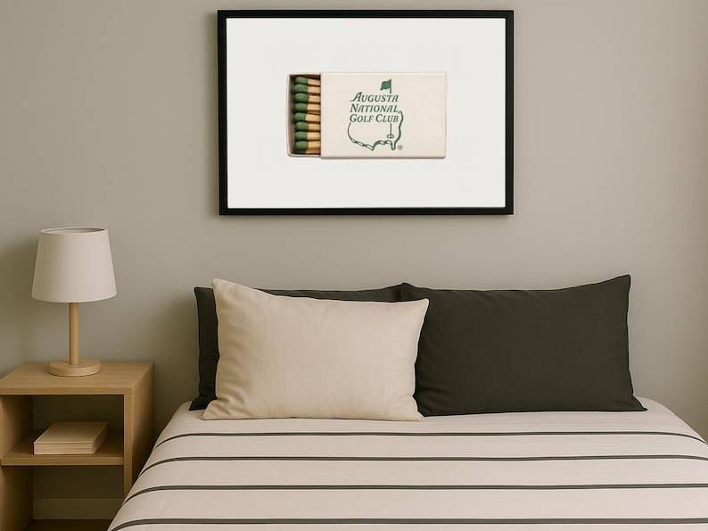 May include: A framed print of a matchbook with the text "Augusta National Golf Club" and a green outline of a golf course. The matchbook has green and white stripes on the side.