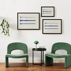 Puede incluir: Dos sillas de terciopelo verde con una mesa auxiliar negra entre ellas. La mesa tiene una l&aacute;mpara verde con una pantalla blanca y dos vasos transparentes. Tres impresiones enmarcadas con dise&ntilde;os abstractos azules y blancos cuelgan de la pared blanca detr&aacute;s de las sillas.