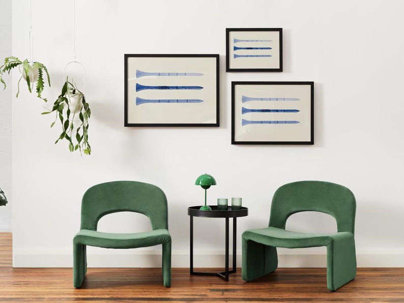 Puede incluir: Dos sillas de terciopelo verde con una mesa auxiliar negra entre ellas. La mesa tiene una l&aacute;mpara verde con una pantalla blanca y dos vasos transparentes. Tres impresiones enmarcadas con dise&ntilde;os abstractos azules y blancos cuelgan de la pared blanca detr&aacute;s de las sillas.