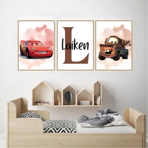 Puede incluir: Tres impresiones enmarcadas con personajes de la película Cars. Una impresión muestra a Rayo McQueen, otra tiene el nombre "Laiken" con una gran letra "L", y la tercera presenta a Mate. Las impresiones tienen un fondo de acuarela.