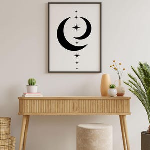 May include: A wooden console table with a light wood finish and a white stool. The table has a black and white print of a crescent moon and stars hanging above it. There are two potted plants on the table, one with a cactus and the other with a palm tree.