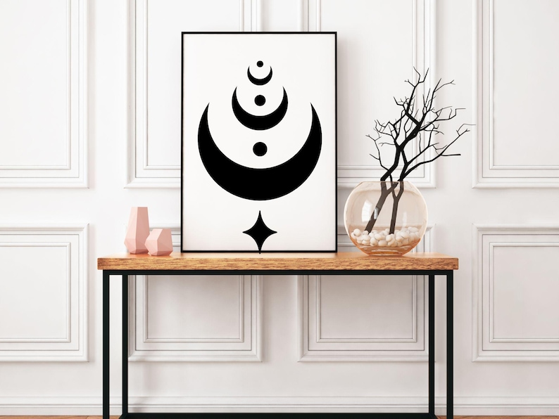 May include: Black and white abstract art print of a crescent moon with a star and circles. The print is framed and displayed on a wooden console table with a vase of branches.