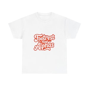 May include: White t-shirt with the text "Footrest for Alphas" in a retro, red script. The text is centered on the front of the shirt. The shirt is a basic crew neck style.