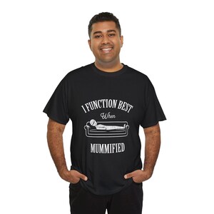 May include: Black t-shirt with the text "I Function Best When Mummified" in white. The design includes a mummy on a couch. The shirt is a casual wear item.