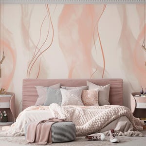May include: A bedroom with a soft, romantic aesthetic. The focal point is a bed with a pink headboard, adorned with pillows and a chunky knit blanket. The walls feature a blush-toned abstract design. Nightstands and a chair complete the scene.