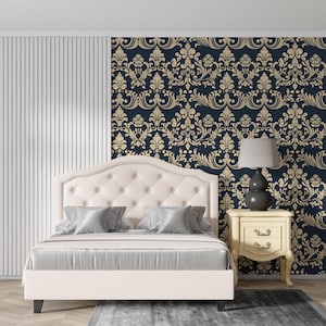 May include: A cream-colored upholstered bed with a tufted headboard and gray pillows and bedding. A nightstand with a lamp sits beside the bed. The wall behind the bed features a navy blue and gold damask pattern.