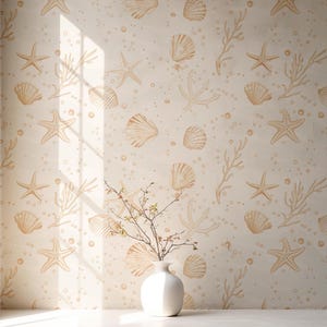May include: A beige wall with a repeating pattern of seashells, starfish, and coral in a light brown color. A white vase with branches is in front of the wall, on a white surface. The sunlight casts shadows on the wall and surface.