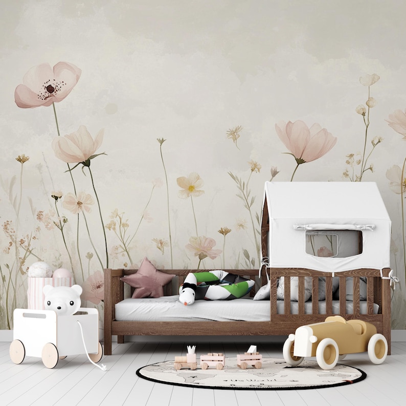 Pu&ograve; includere: Una cameretta per bambini con un letto in legno, una struttura a casetta bianca e un'auto giocattolo gialla. La stanza presenta una carta da parati floreale con fiori rosa e crema. Sono visibili anche un giocattolo a forma di orso bianco e un cuscino a forma di stella.
