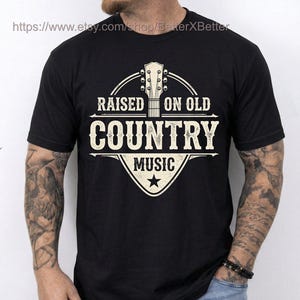 May include: Black t-shirt with a cream-colored graphic that reads "RAISED ON OLD COUNTRY MUSIC." The design features a guitar headstock and a star. The shirt is short-sleeved.