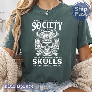 Puede incluir: Camiseta azul abeto con un gr&aacute;fico que presenta una calavera con un casco con cuernos, huesos cruzados y el texto "THE PROBLEM WITH SOCIETY TODAY IS THAT NO ONE DRINKS FROM THE SKULLS OF THEIR ENEMIES ANYMORE."