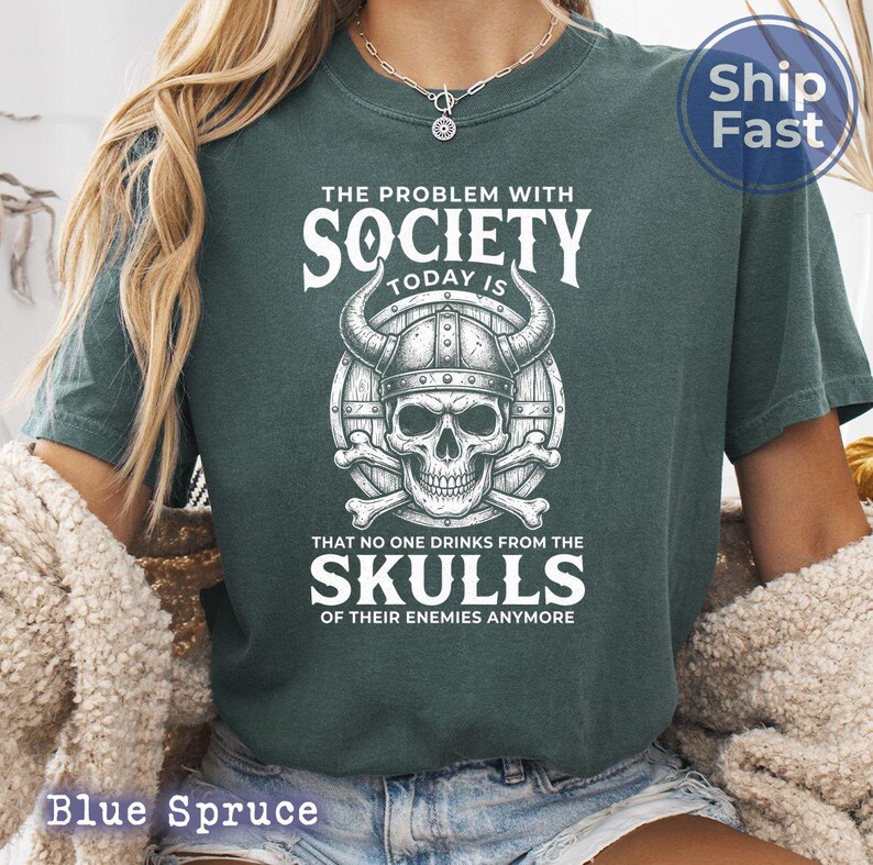 Puede incluir: Camiseta azul abeto con un gr&aacute;fico que presenta una calavera con un casco con cuernos, huesos cruzados y el texto "THE PROBLEM WITH SOCIETY TODAY IS THAT NO ONE DRINKS FROM THE SKULLS OF THEIR ENEMIES ANYMORE."
