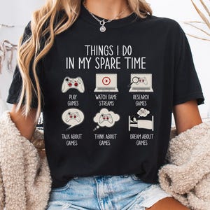 Puede incluir: Una camiseta negra con el texto "Things I do in my spare time" y una lista de actividades relacionadas con los videojuegos, que incluyen "Play Games", "Watch Game Streams", "Research Games", "Talk About Games", "Think About Games" y "Dream About Games".