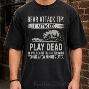 May include: A black short-sleeve t-shirt featuring white text that reads: BEAR ATTACK TIP: IF ATTACKED, PLAY DEAD. IT WILL BE GOOD PRACTICE FOR WHEN YOU DIE A FEW MINUTES LATER. The graphic includes a line drawing of a bear standing over a person.