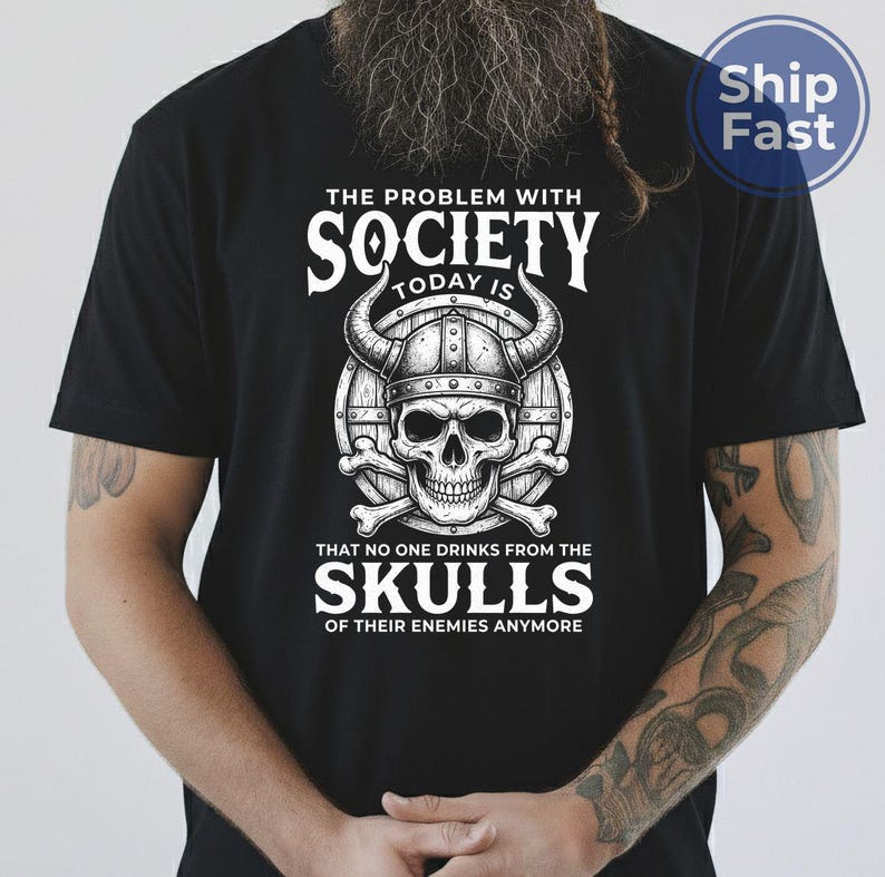 Puede incluir: Camiseta negra con un dise&ntilde;o gr&aacute;fico que presenta una calavera con un casco con cuernos, huesos cruzados y el texto "THE PROBLEM WITH SOCIETY TODAY IS THAT NO ONE DRINKS FROM THE SKULLS OF THEIR ENEMIES ANYMORE."