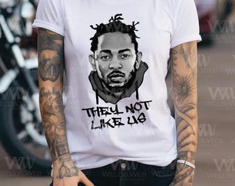 May include: White t-shirt featuring a black and white portrait of a man with dreadlocks. Below the portrait, the text reads "THEY NOT LIKE US" in a graffiti-style font. The shirt is a classic crew neck.
