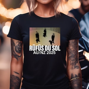 May include: Black t-shirt with a graphic of three figures in black suits standing on a light brown background. The text "RÜFÜS DU SOL AU/NZ 2025" is printed in white below the graphic.