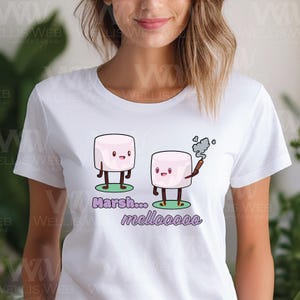 May include: White t-shirt featuring a cartoon design of two marshmallows. One marshmallow is holding a lit stick, with the text "Marsh... mellooooo" in purple below. The design is on a green base.