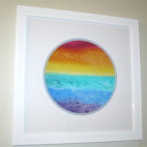 May include: A framed circular painting with a colorful abstract design. The painting features a gradient of colors, starting with red at the top and transitioning to yellow, green, blue, and purple at the bottom. The painting is framed in a white frame.