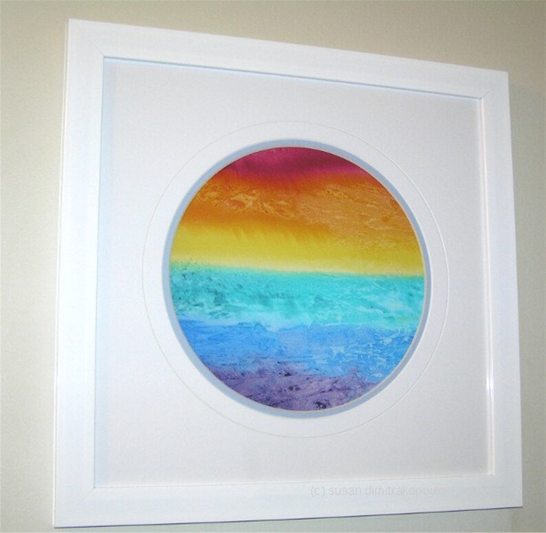 May include: A framed circular painting with a colorful abstract design. The painting features a gradient of colors, starting with red at the top and transitioning to yellow, green, blue, and purple at the bottom. The painting is framed in a white frame.