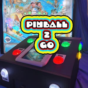 Puede incluir: Una máquina de pinball negra con el texto "PINBALL 2 GO" en un marco colorido. La máquina tiene botones rojos, verdes y amarillos, una pantalla y botones de monedas y de inicio. La máquina de pinball tiene un tema de tiburón.