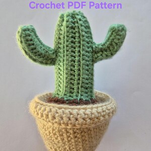May include: A crochet PDF pattern featuring a green cactus with two arms planted in a beige pot. The cactus has a ribbed texture and sits in a round, textured beige container. The text Crochet PDF Pattern is displayed above the cactus.
