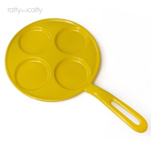 May include: Yellow cast iron skillet with four round indentations for cooking individual portions of food.