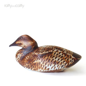 May include: A ceramic duck figurine with brown and white speckled glaze. The duck is lying on its side with its head turned to the left.