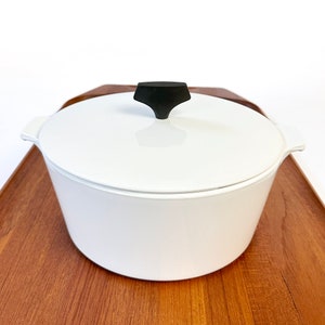 May include: White ceramic pot with a black knob on the lid. The pot is sitting on a wooden surface.