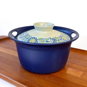 May include: A blue ceramic casserole dish with a white lid featuring a floral design in shades of blue, green, and yellow.