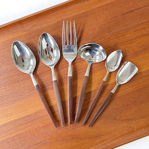 May include: A set of six stainless steel serving utensils with dark brown wooden handles. The collection includes a solid spoon, a slotted spoon, a four-tined fork, a small ladle, a small spoon, and a small square-edged serving utensil.