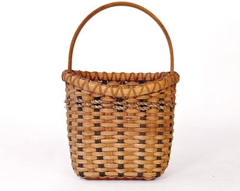 May include: A handcrafted woven basket with a rounded handle. The basket features a natural brown color with dark brown accents in a checkered pattern. A rope-like detail encircles the basket near the top, adding a rustic touch.