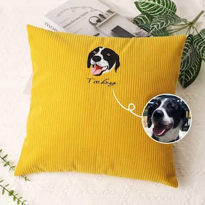 May include: Mustard yellow corduroy cushion featuring an embroidered dog portrait. The dog is black and white with its tongue out. The name "Toby" is embroidered below the dog's face. A smaller photo of the dog is in the lower right corner.