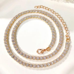 Peut inclure: Un collier tennis dor&eacute; orn&eacute; de pierres de zircone cubique claires et &eacute;tincelantes. Le collier est dot&eacute; d'une cha&icirc;ne d&eacute;licate et d'un fermoir s&ucirc;r. Les pierres sont serties de pr&egrave;s, cr&eacute;ant une ligne continue de brillance. Le collier est con&ccedil;u pour &ecirc;tre port&eacute; autour du cou.