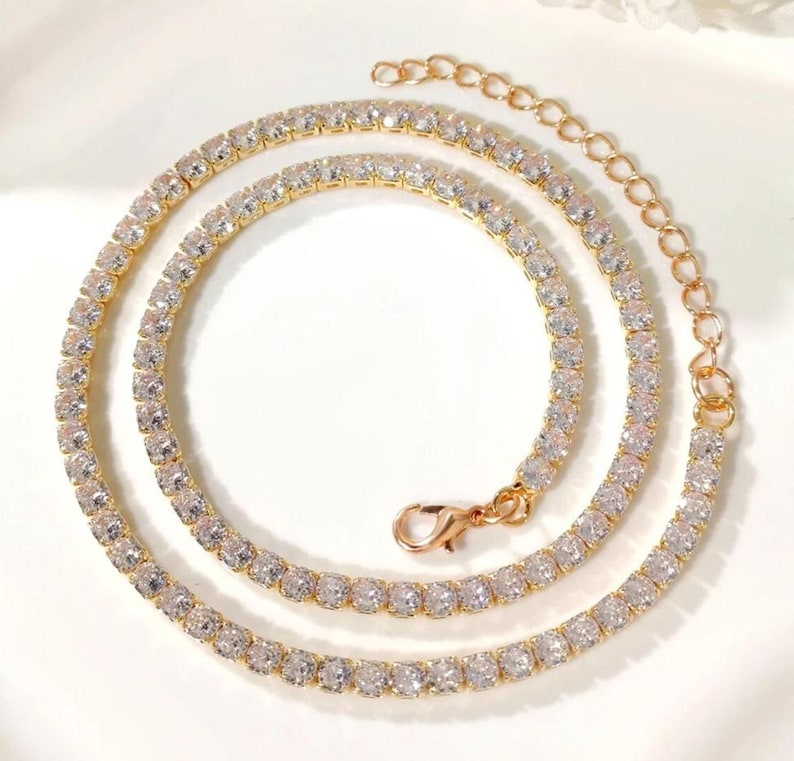 Peut inclure: Un collier tennis dor&eacute; orn&eacute; de pierres de zircone cubique claires et &eacute;tincelantes. Le collier est dot&eacute; d'une cha&icirc;ne d&eacute;licate et d'un fermoir s&ucirc;r. Les pierres sont serties de pr&egrave;s, cr&eacute;ant une ligne continue de brillance. Le collier est con&ccedil;u pour &ecirc;tre port&eacute; autour du cou.