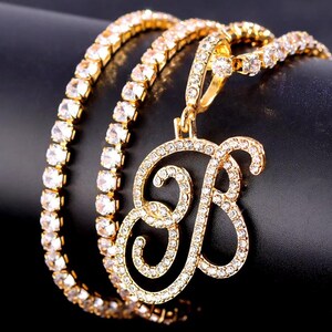 Peut inclure: Collier dor&eacute; avec un pendentif en forme de lettre "B", incrust&eacute; de cristaux transparents. La cha&icirc;ne du collier est &eacute;galement orn&eacute;e de cristaux. Le bijou est pr&eacute;sent&eacute; sur un fond sombre.