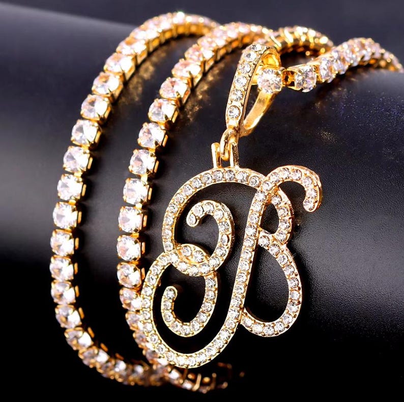 Peut inclure: Collier dor&eacute; avec un pendentif en forme de lettre "B", incrust&eacute; de cristaux transparents. La cha&icirc;ne du collier est &eacute;galement orn&eacute;e de cristaux. Le bijou est pr&eacute;sent&eacute; sur un fond sombre.