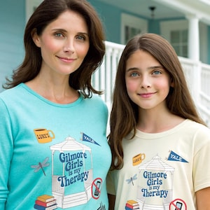 May include: Two people wearing light blue and cream colored t-shirts with a graphic print of a gazebo, a dragonfly, books, a coffee cup, and the text "Gilmore Girls is my Therapy". The text "Luke's" and "Yale" are also printed on the shirts.