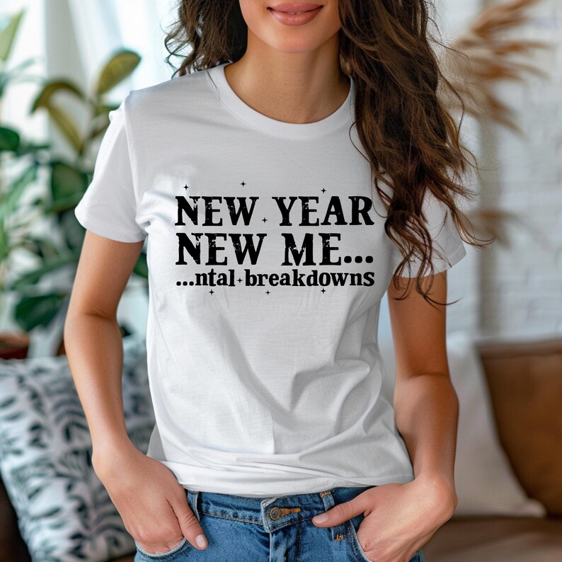 May include: A white short-sleeved t-shirt featuring black text that reads NEW YEAR NEW ME... ...ntal breakdowns, accented with small star symbols. The shirt has a crew neckline and is paired with blue denim jeans, creating a casual look.