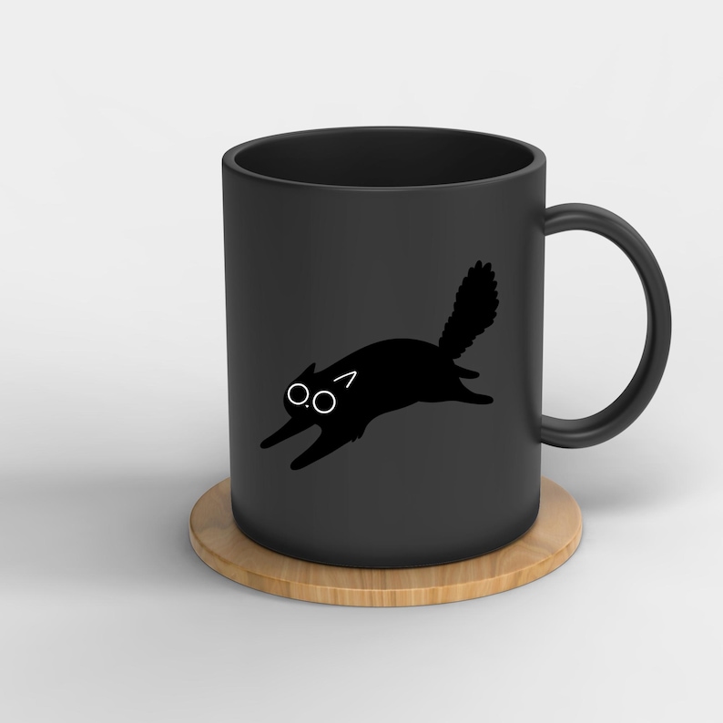 May include: Black ceramic mug with a black cat silhouette design. The cat is depicted in a running pose with a fluffy tail and wide eyes. The mug sits on a round, light brown coaster.