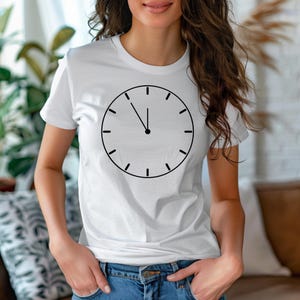 May include: White t-shirt with a black clock face design. The clock face shows the time as 12 o'clock.