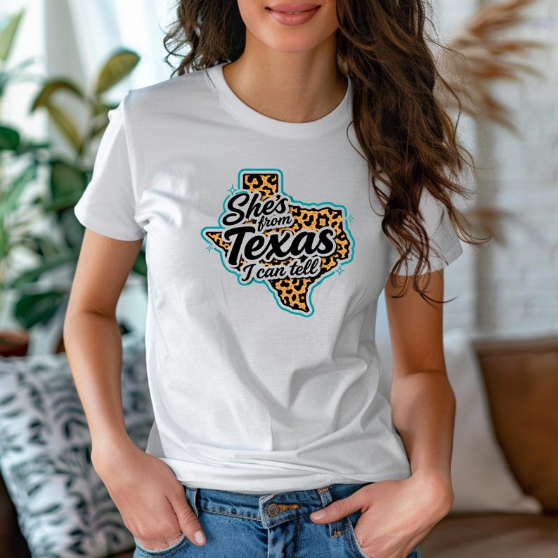 May include: White t-shirt with a graphic of the state of Texas and the text "She's from Texas I can tell". The Texas outline is filled with a leopard print pattern, outlined in teal, and the text is in black.